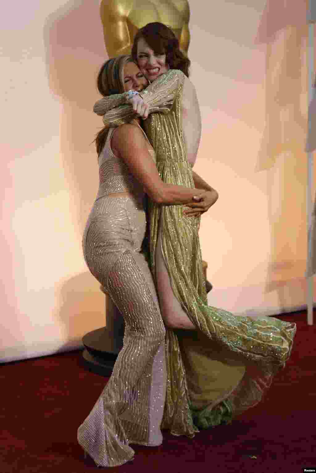 Les atrices Jennifer Aniston (G) et Emma Stone s'étreignent sur le tapis rouge à leur arrivée à la cérémonie des 87e Oscars à Hollywood, Californie, le 22 février 2015