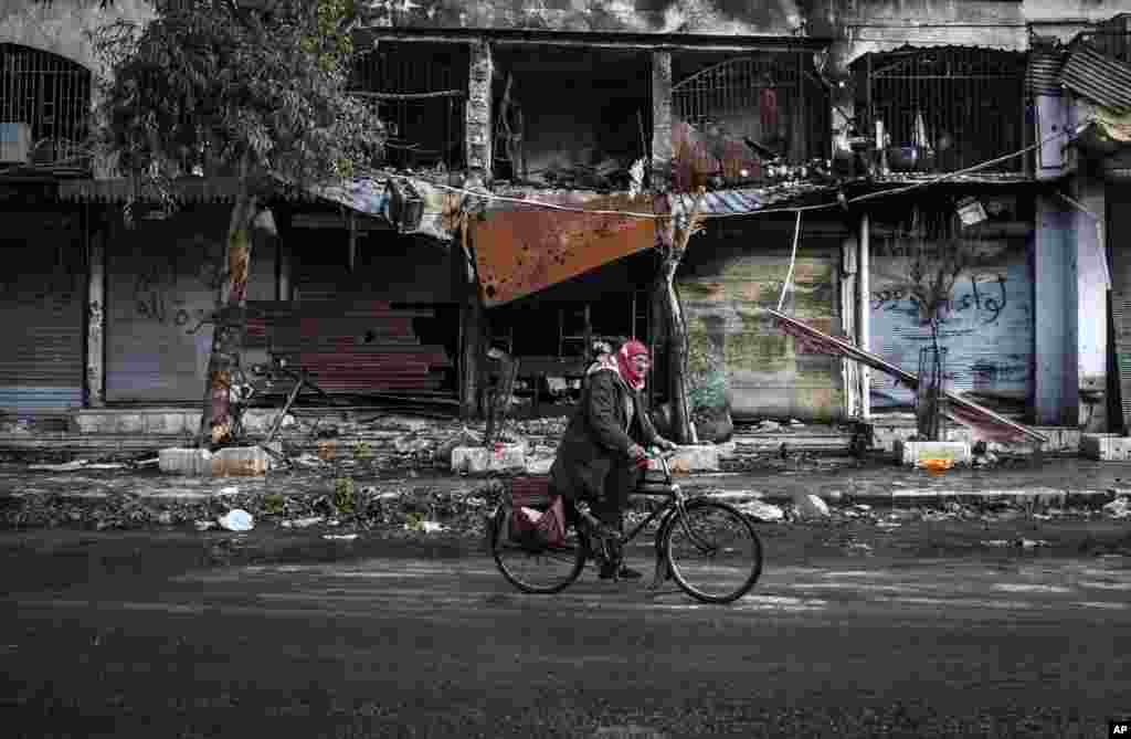 A man rides his bicycle past buildings damaged by shelling in the old city of Aleppo, Syria, January 6, 2013.