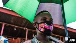 Mchuuzi katika soko la Nakasero mjini Kampala Uganda akiwa amevaa barakoa na kushika mwamvuli.(Photo by SUMY SADURNI / AFP)